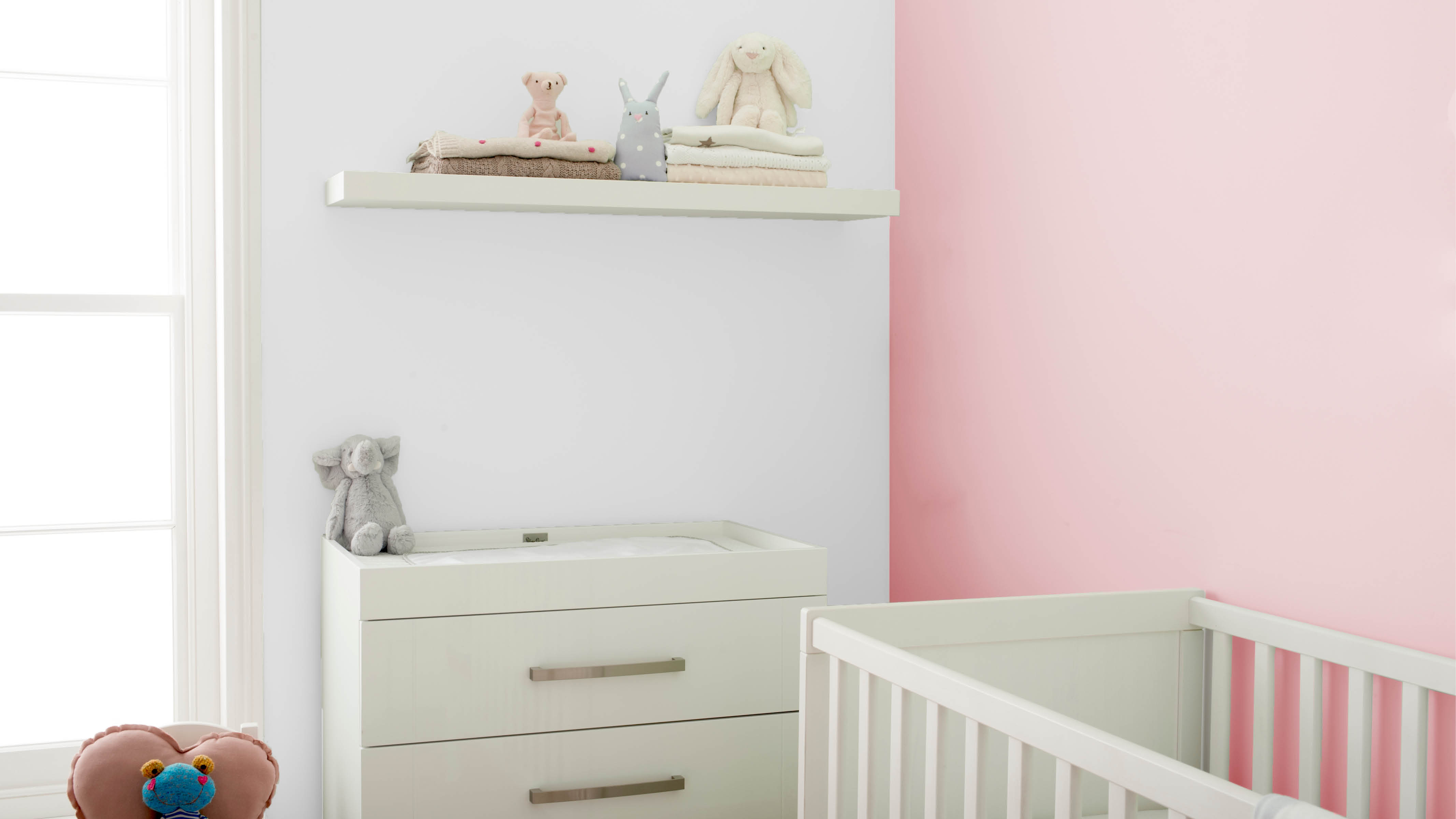 Pink nursery with floating shelves A white cabinet and a set of floating shelves are a great place to stash nappies and other baby care items.